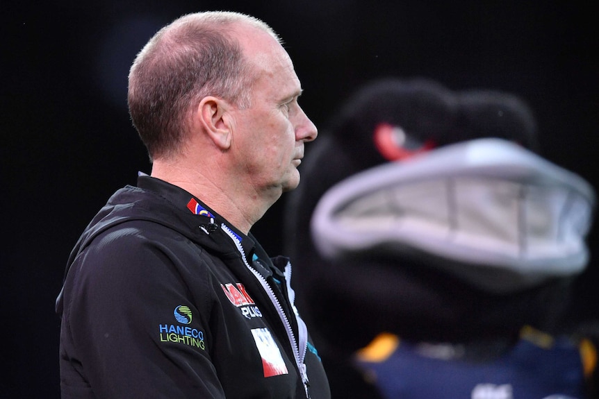 Ken Hinkley looks off in the distance with a giant crow mascot in the background.