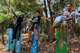 Three students hold hands while sitting on letters of a sign outside Milpera State High School at Chelmer in Brisbane.