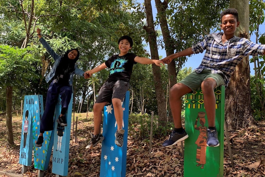 Three students hold hands while sitting on letters of a sign outside Milpera State High School at Chelmer in Brisbane.