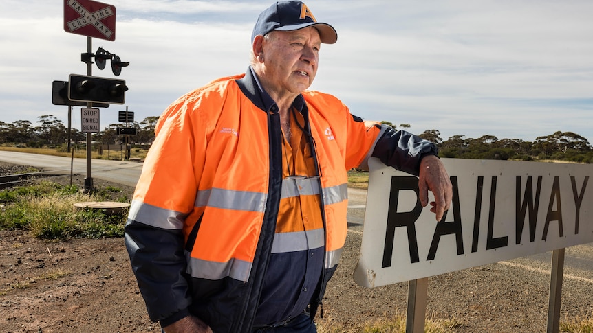 A man wearing high-vis workwear leaning on a railway sign.