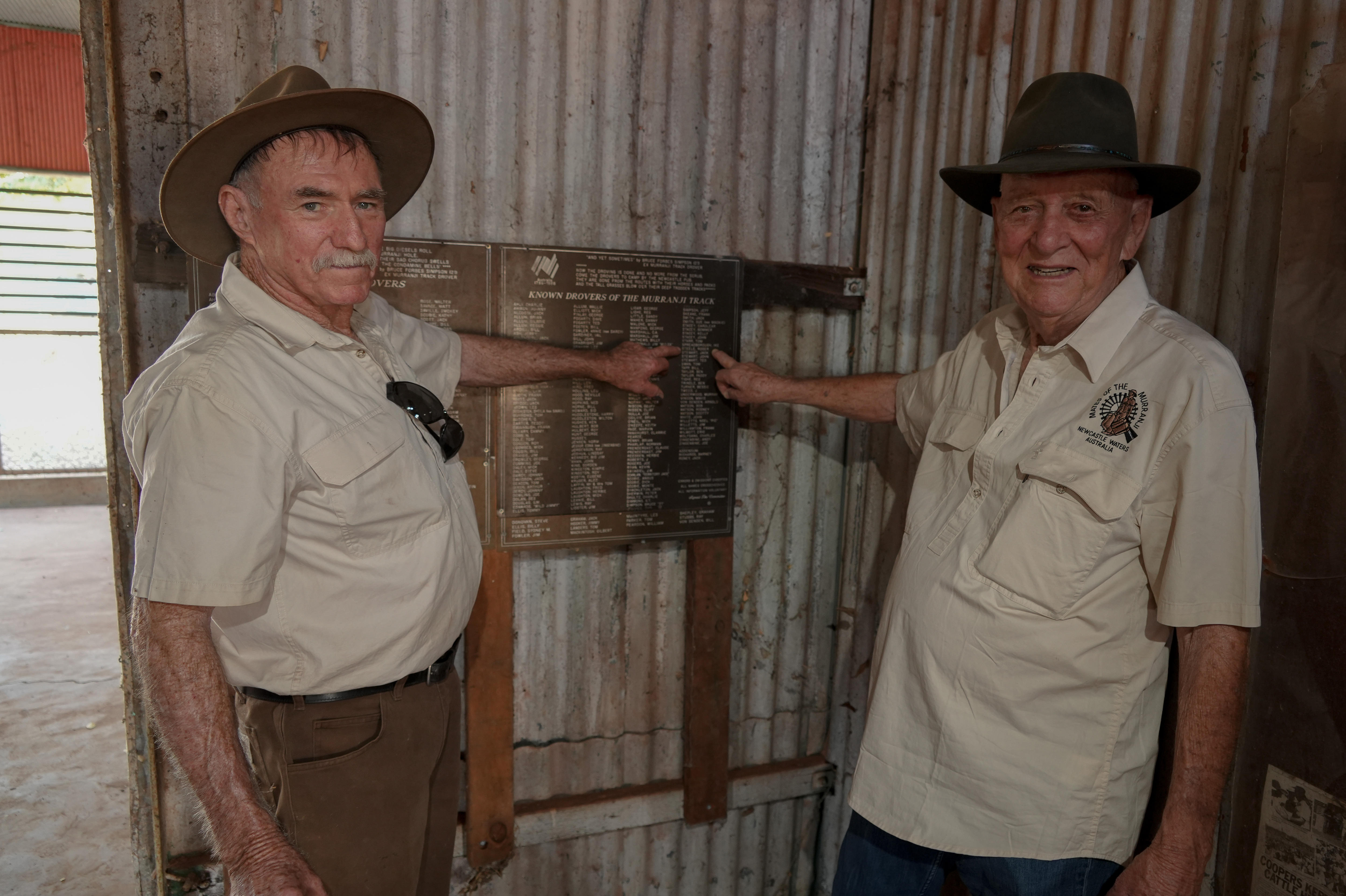 Two men stand facing the camera and point at a plaque.