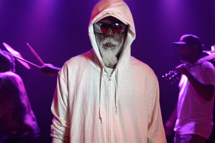 Man with sunglass and hoodie standing in front of purple screen 