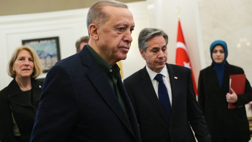 Recep Tayyip Erdoğan talks to Antony Blinken while surrounded by other men.
