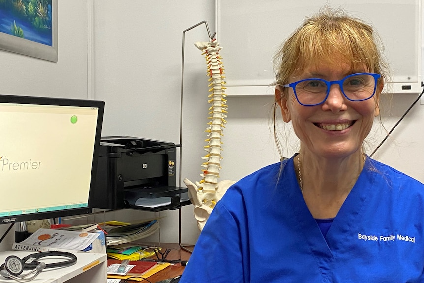 Dr Jennie Wright, GP, sits in her office in Adelaide, smiling at the camera with a model spine and computer in the background