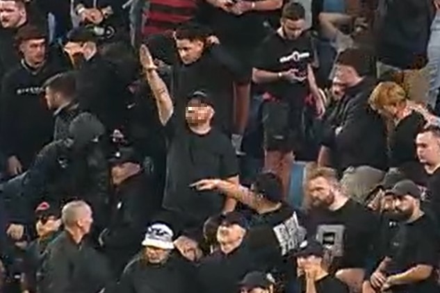 Football fan, stading in a grandstand, appearing to make a Nazi salute gesture