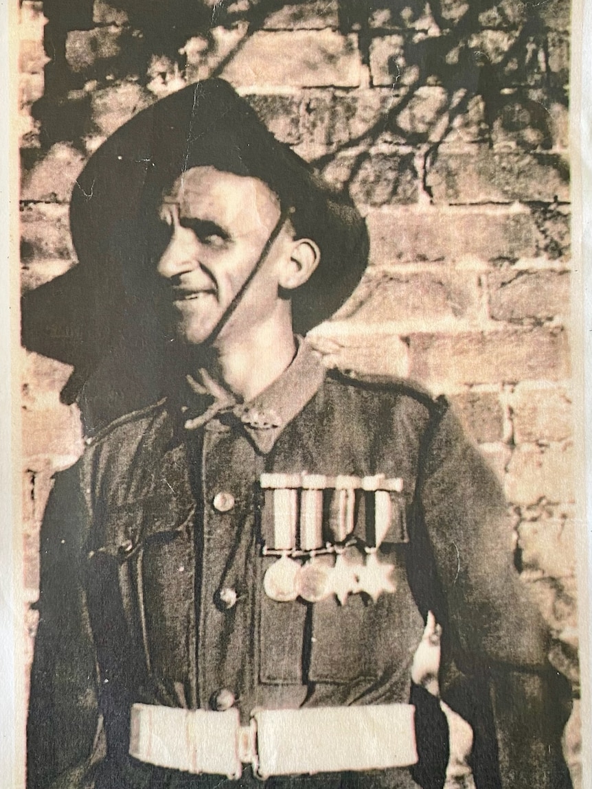 A man in military uniform stands in front of a brick wall