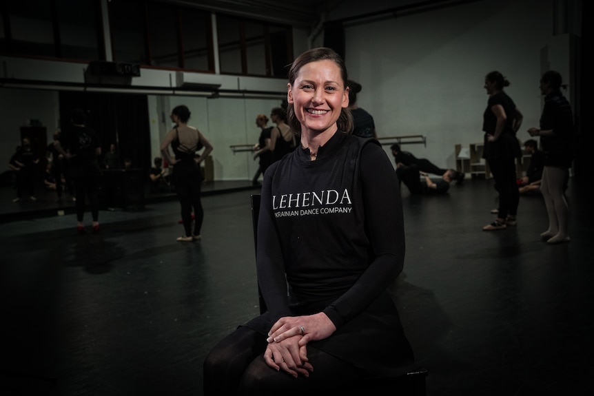 Melanie Moravski Dechnicz smiles at the camera in a dance studio with people in leotards behind her.