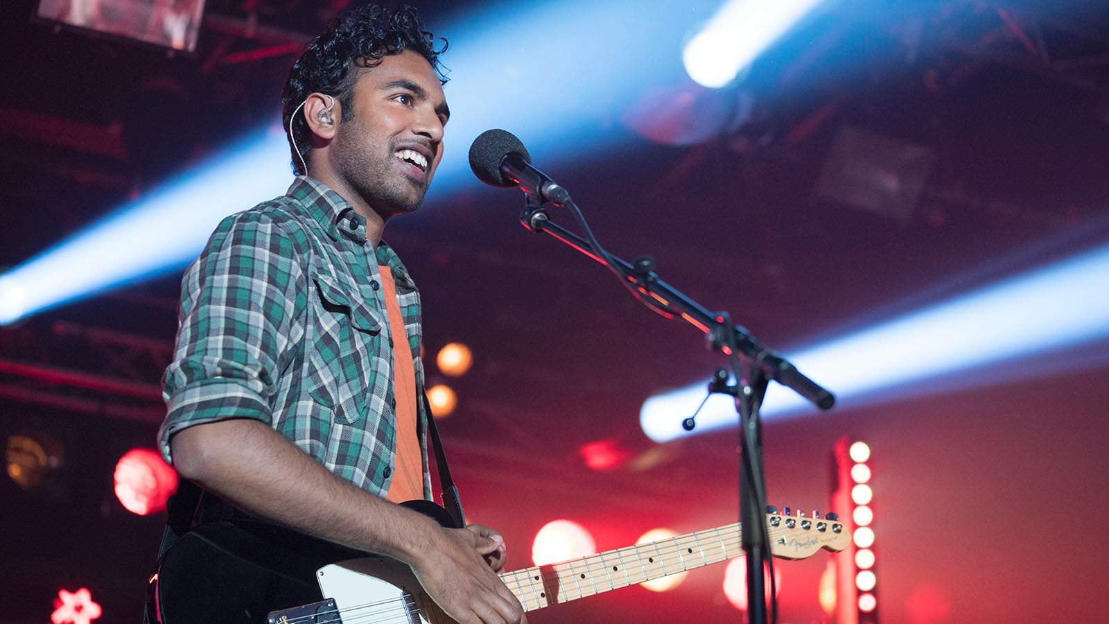 Patel stands on a stage, guitar slung on shoulder, smiling out to the crowd.