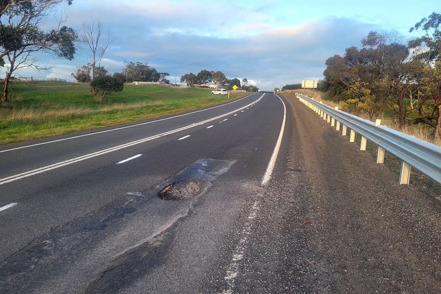 A large pothole around a bend in a highway.