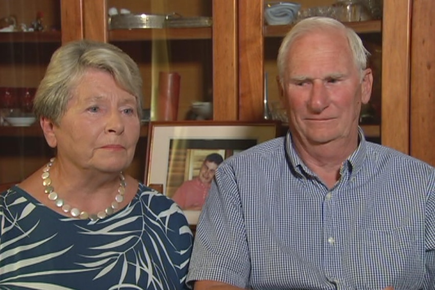 A woman and a man sitting in front of a wall cabinet.