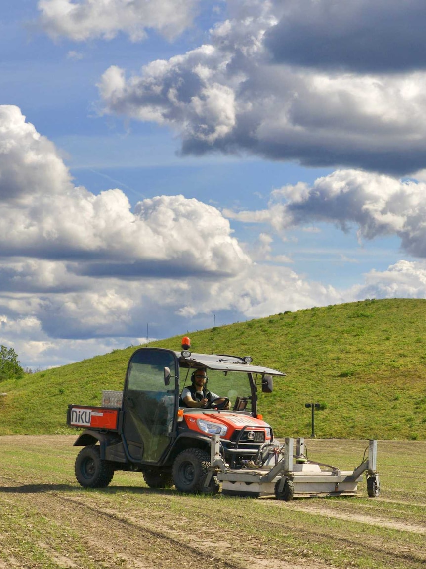 A man sits inside an enclosed quad bike with a large metal attachment on the front.