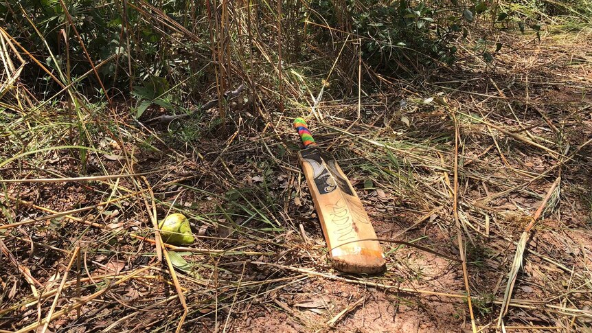A cricket bat and a piece fruit lay by the roadside where a car rolled and killed three people.