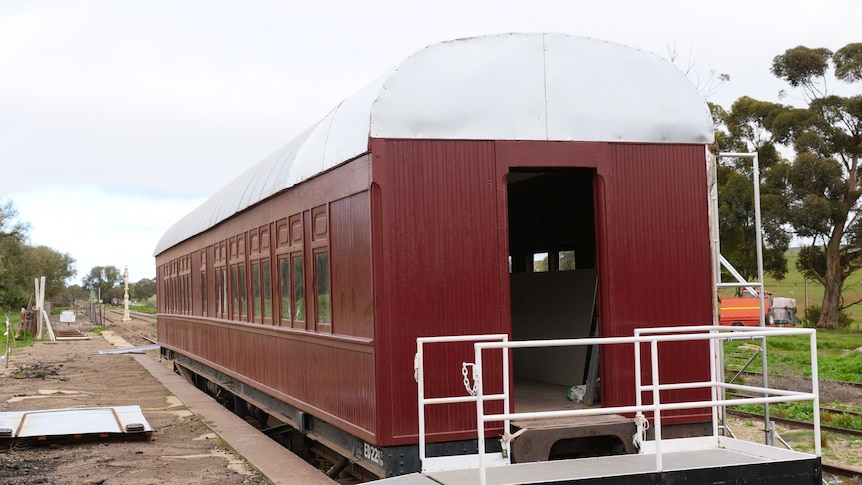 A maroon painted carriage with a metal roof sits on some old rail tracks.