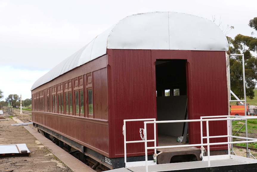 A maroon painted carriage with a metal roof sits on some old rail tracks.