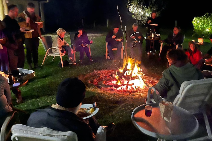 A group of people chatting and eating around a fire under the stars