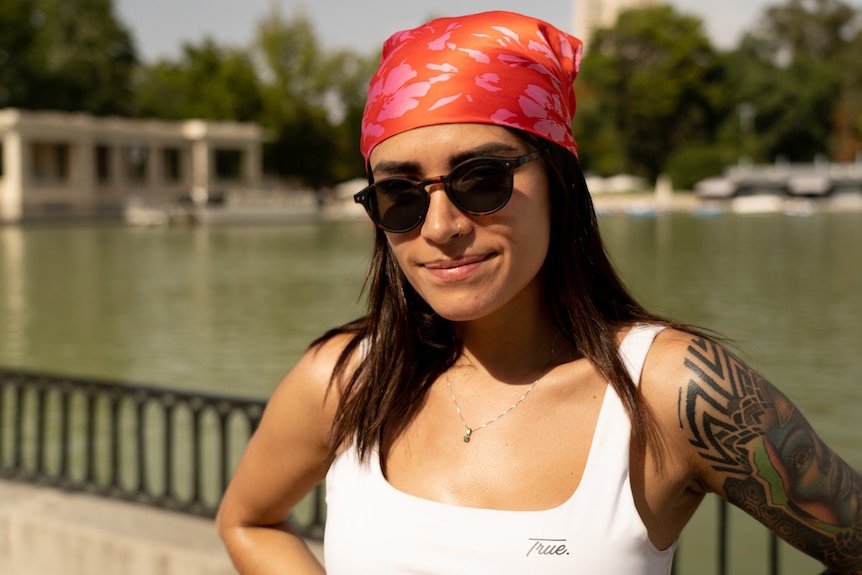 Mujer joven con un pañuelo rojo y rosa en la cabeza y gafas de sol junto a un cuerpo de agua