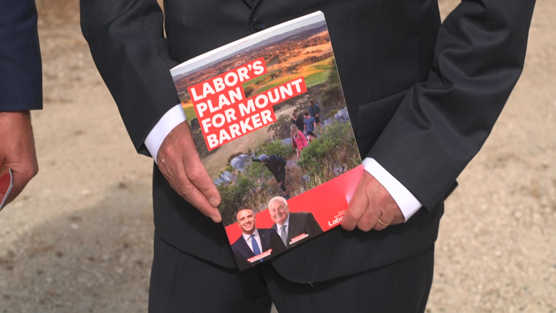 Un hombre con traje sostiene un folleto titulado: Plan laborista para Mount Barker