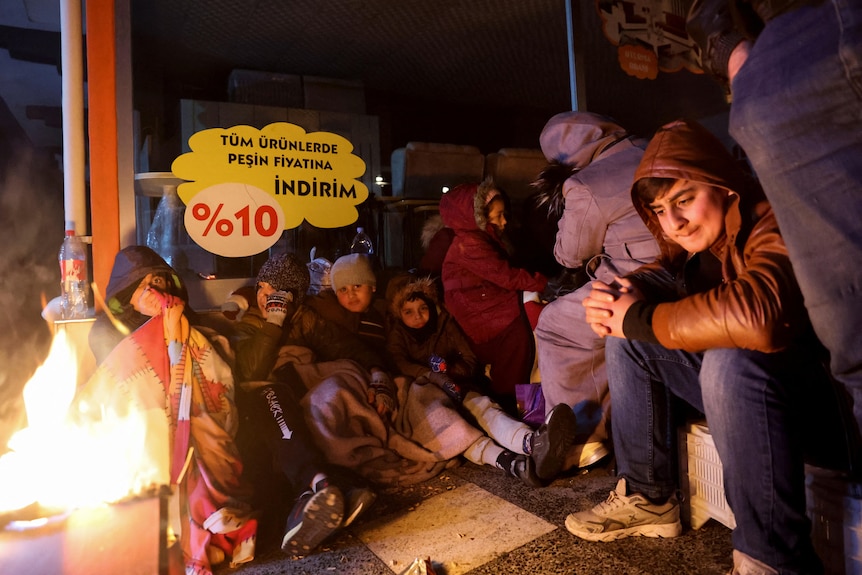 Youngsters sit around a fire near the site of a collapsed hospital, following an earthquake in Iskenderun