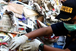 A customs officer standing in front of a giant pile of rubbish