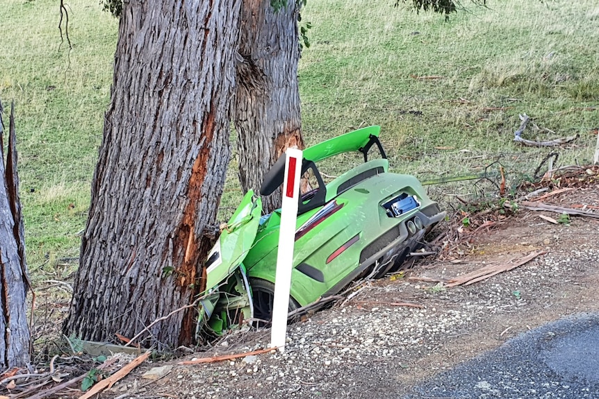A green car lies smashed between two gum trees