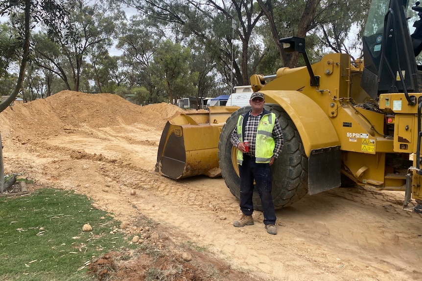 A man in a yellow vest standing in front of a tractor with dirt in the background.