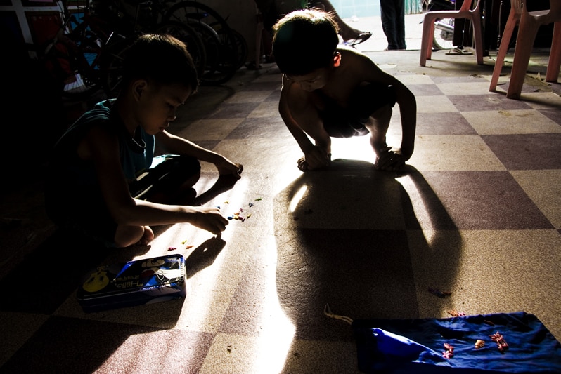 Two children squat down on the floor at an orphanage in Phnom Penh, Cambodia.