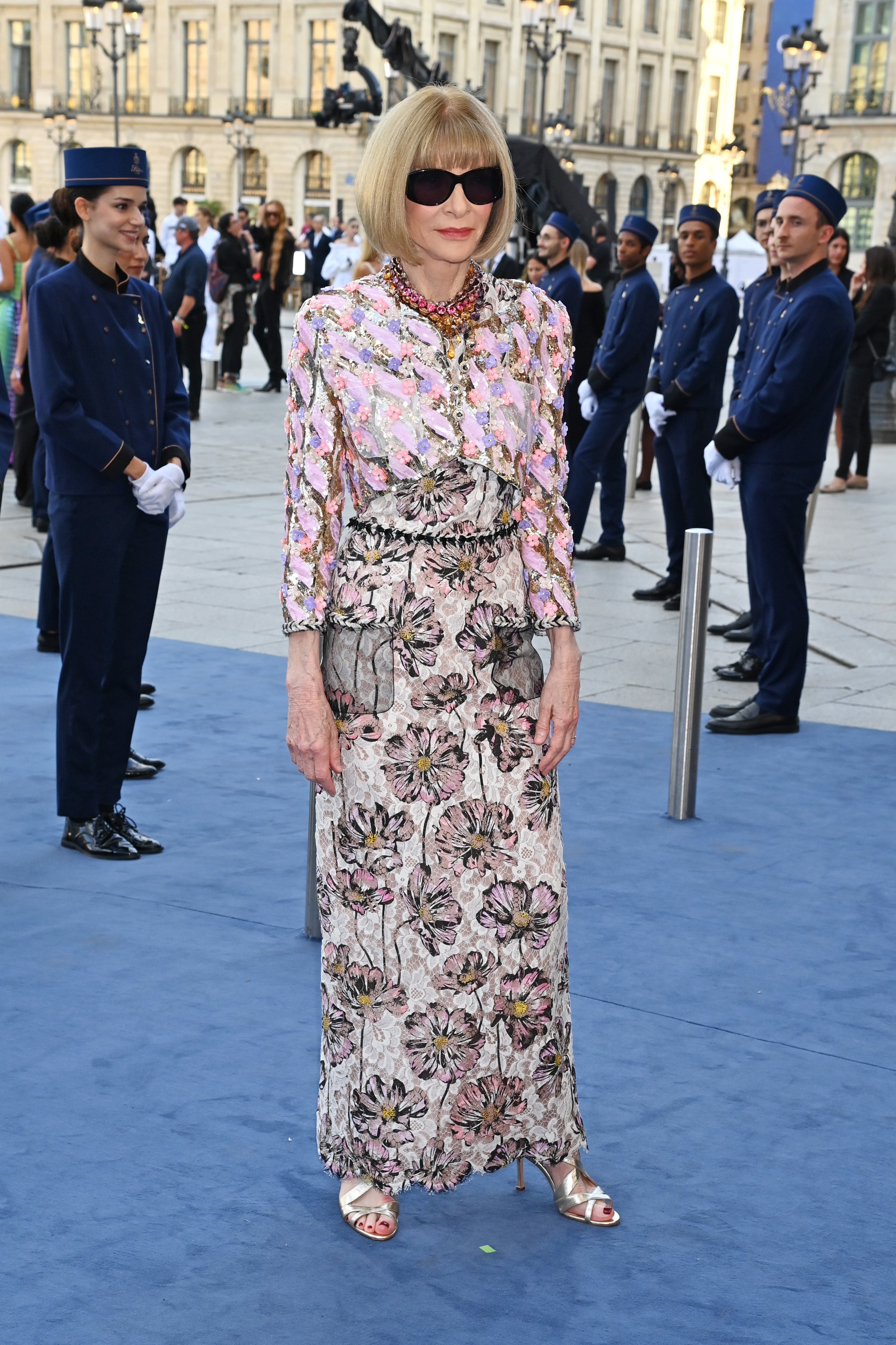 Anna Wintour poses at an event in dark sunglasses and a matching skirt and blazer