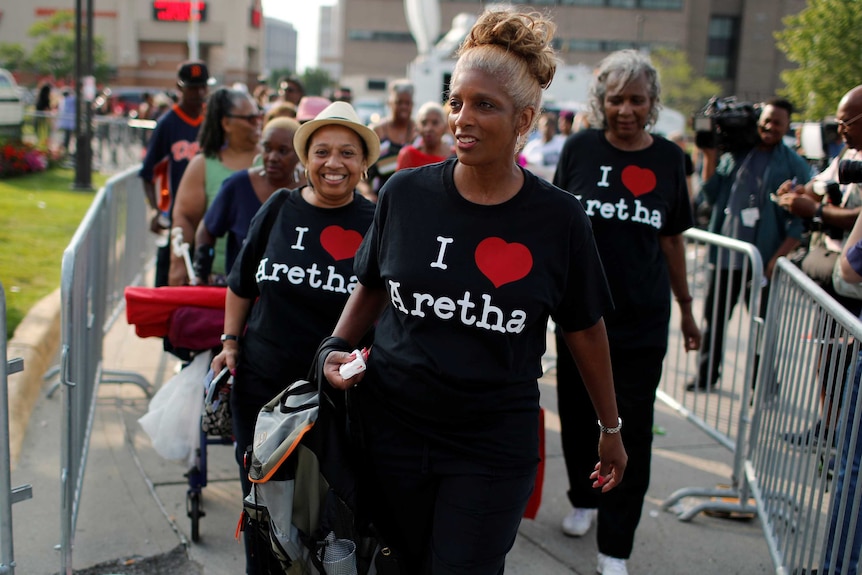 People with t-shirts saying "I love Aretha" wait in a line.