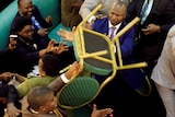 A Ugandan lawmaker throws a chair at another man in parliament while another lawmaker is held back by four others.