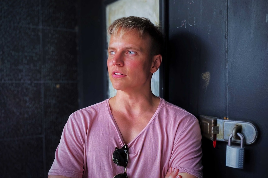 A portrait of a man with blonde hair wearing a salmon coloured shirt