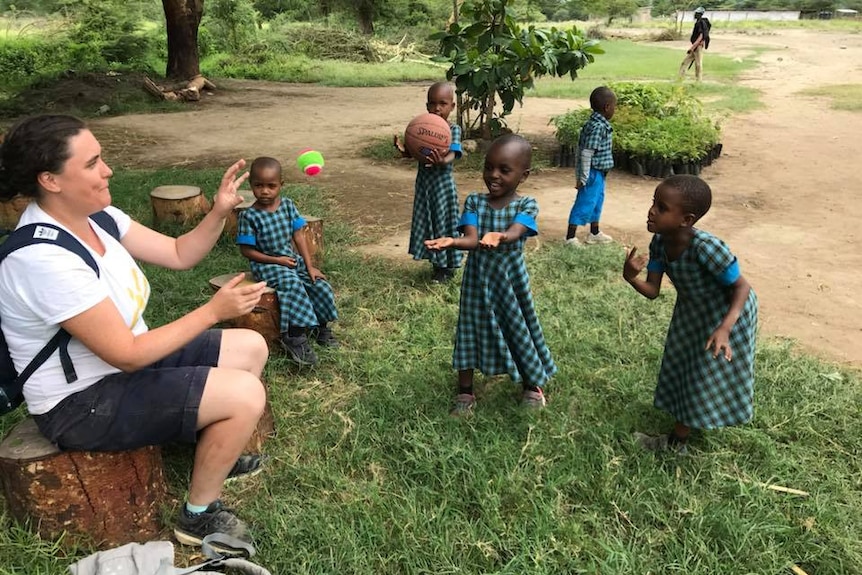 Tanzanian children throw a tennis ball to a woman