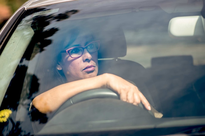 Sandy behind the drivers seat of her car, driving.