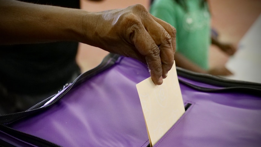 A hand placing a ballot in a voting box.