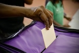 A hand placing a ballot in a voting box.