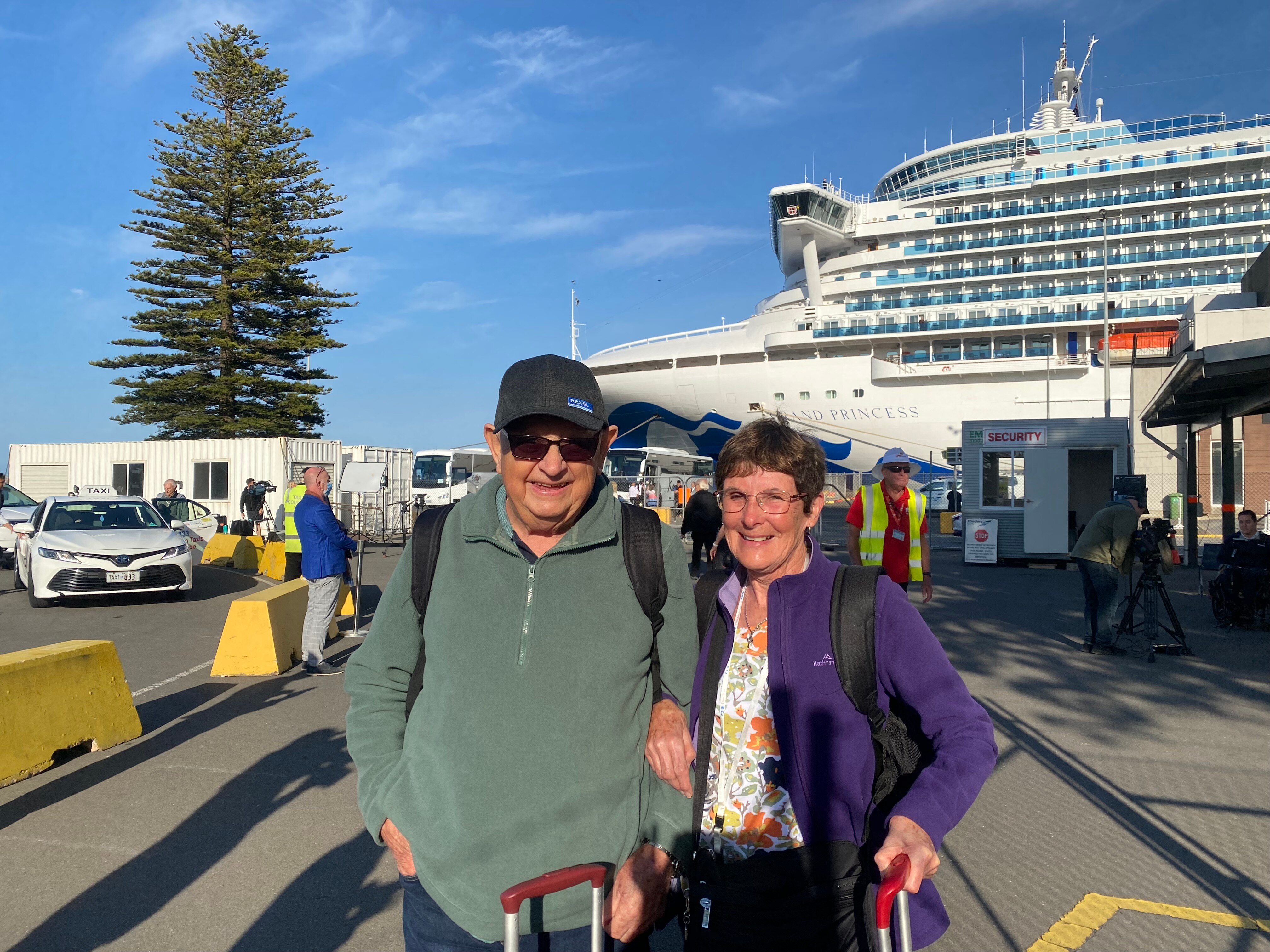 A man and a woman with luggage standing in front of a cruise ship
