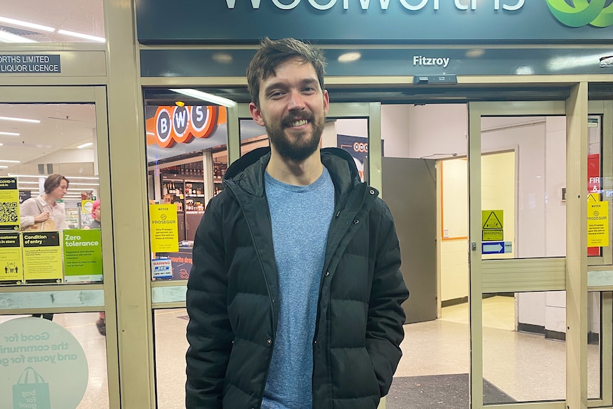 a man smiling outside a supermarket at dusk