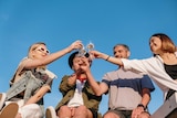 Two women and two men toast at an outdoor party, a summer barbecue that caters for vegans.