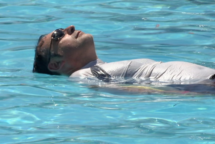 A man floats on his back in a swimming pool.