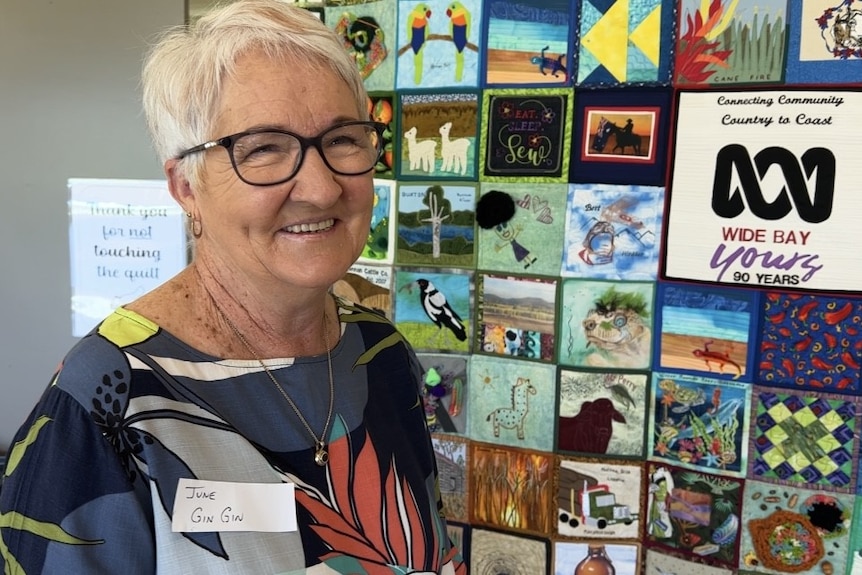 A wom,an in black glasses smiles in front of a quilt 