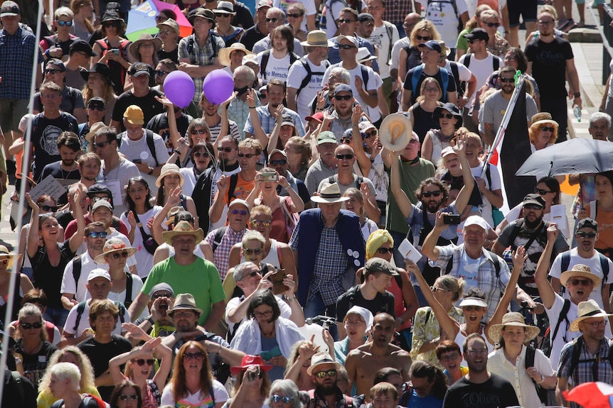 A group of people clap, cheer and raise their hands as they march together along a wide road in the sunshine.