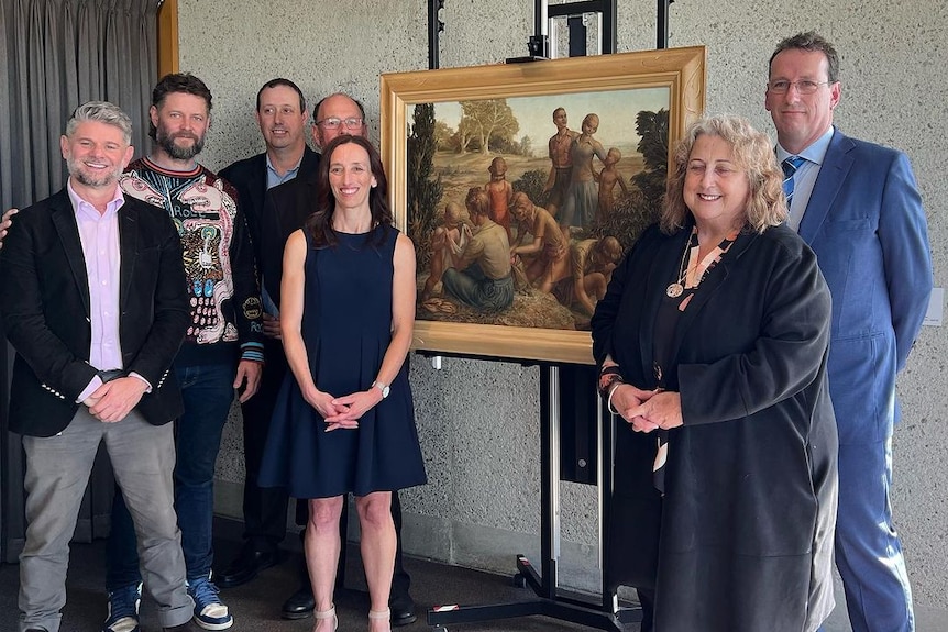 A group of people stand next to the BushWalkers painting on an easel.