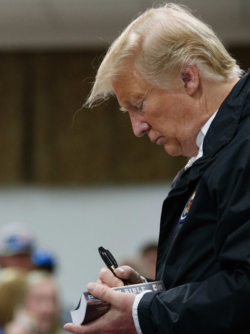 US President Donald Trump looks down at a paperback Bible as he signs it with a big felt pen.