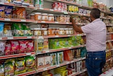 A man standing against supermarket shelves with his back to the camera, rearranging products.