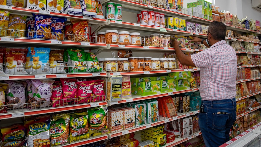 A man standing against supermarket shelves with his back to the camera, rearranging products.