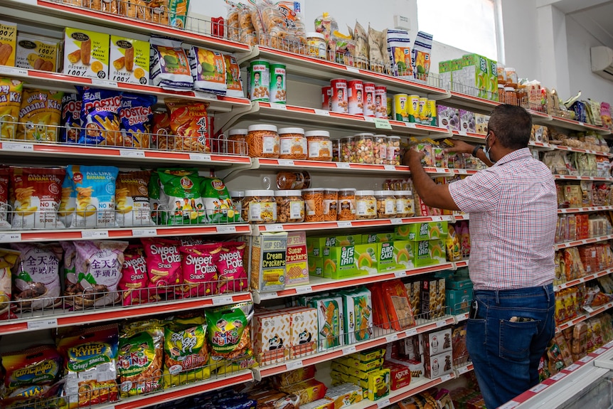 A man standing against supermarket shelves with his back to the camera, rearranging products.