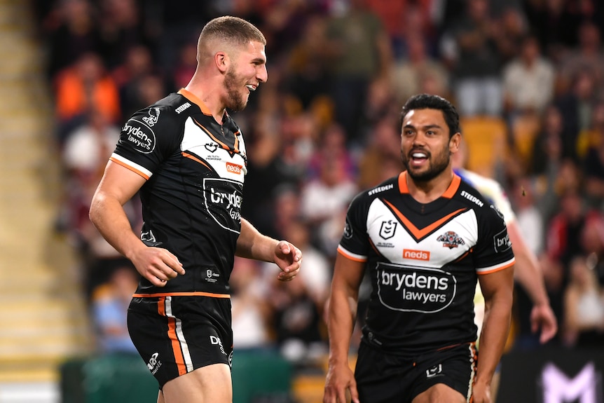 An NRL player grins as he looks at a Wests Tigers teammate after scoring a try in Magic Round.