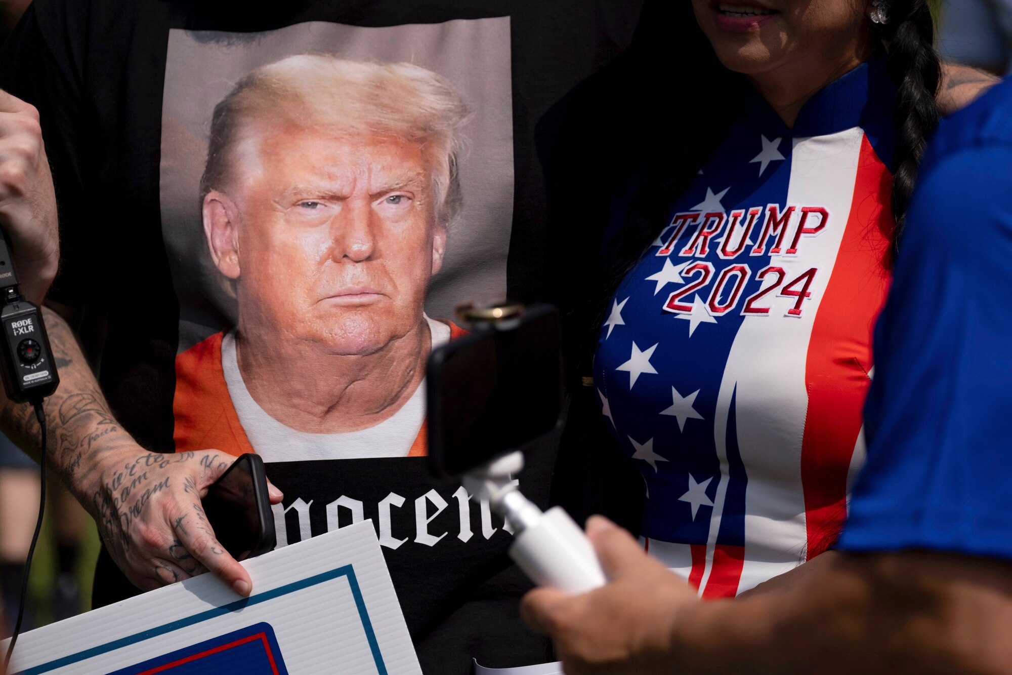 A close-up on two people's Tshirts shows one with Donald Trump's face and the word INNOCENT