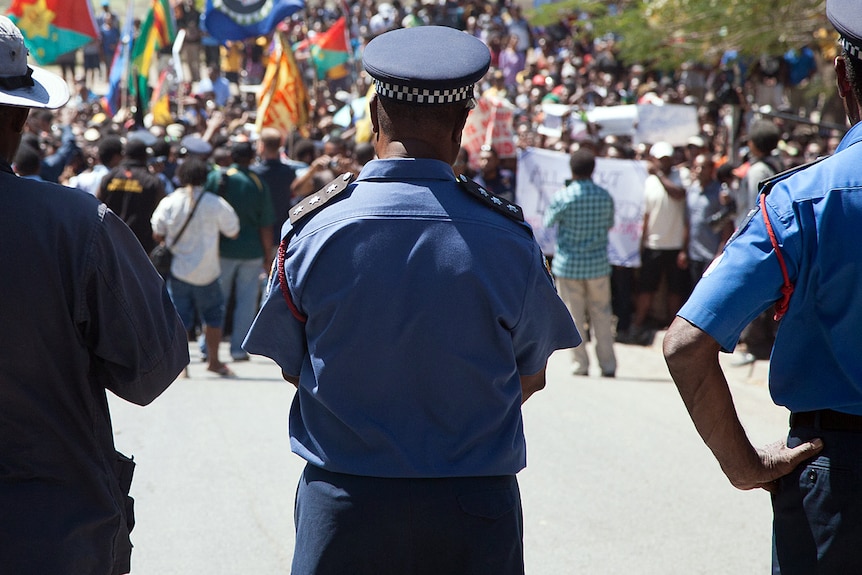 Papua New Guinea police officers watch on as hundreds of students marched towards the university gate in Port Moresby