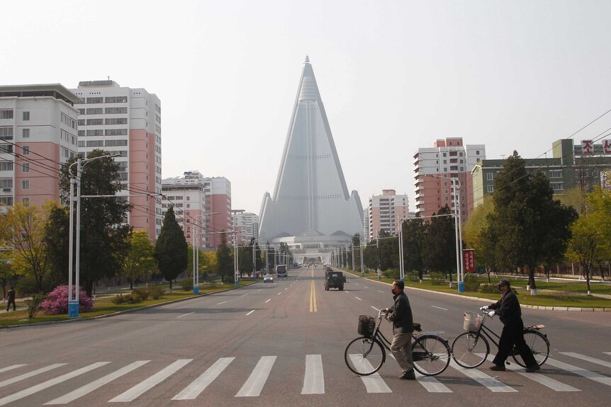 People wearing face masks cross a road in front of the Ryugyong Hotel in Pyongyang.
