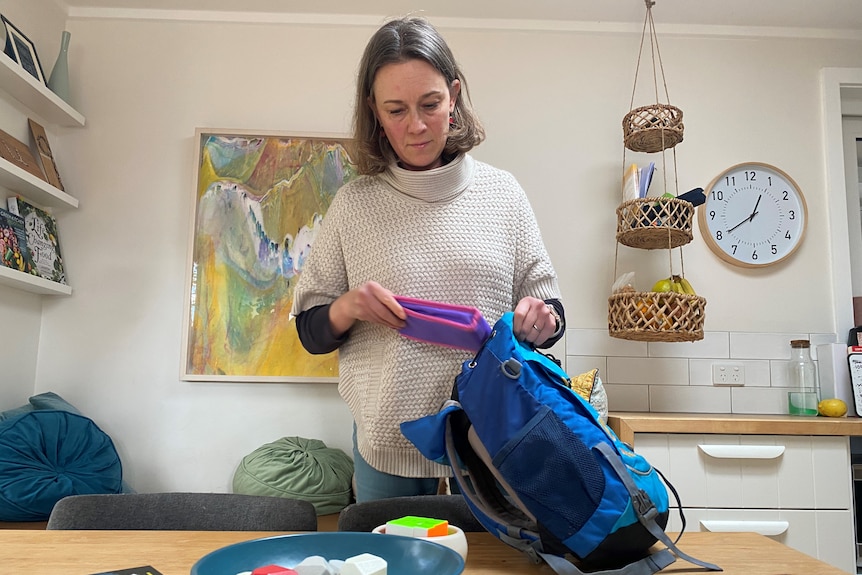 A woman puts a children's lunchbox into a backpack